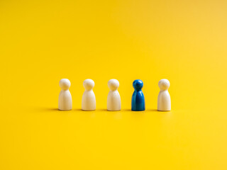 The blue one, different standing out of the group of white peg dolls, people symbols, on yellow background. Stand out from the crowd, leadership, unique, influencer, talent people, difference concept.