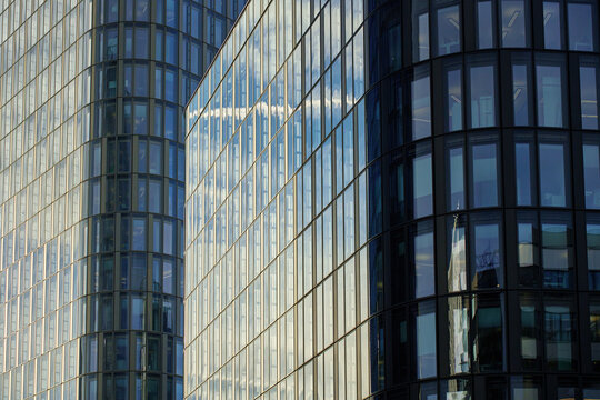 Modern glass skyscrapers reflecting blue sky and surrounding city. High-rise office buildings with curved glass facades. Contemporary architecture in city business district - Powered by Adobe