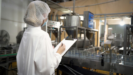 A woman wearing a white lab coat and a hat is writing on a clipboard in a factory. Concept of order and organization, as the woman is likely keeping track of inventory or other important information