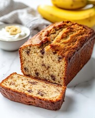 Freshly baked banana bread loaf with chocolate chips served on a white marble surface with bananas in the background