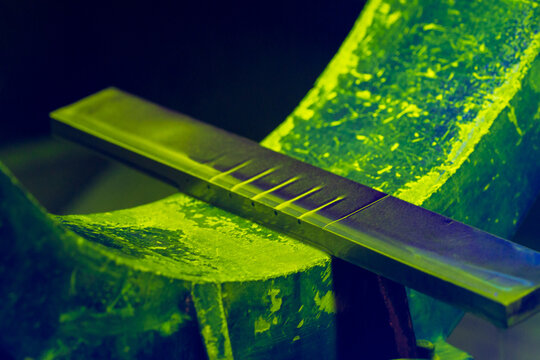 Quality Control Test Block for Magnetic Particle Inspection. Fluorescent green MPI reference standard with defects under ultraviolet illumination