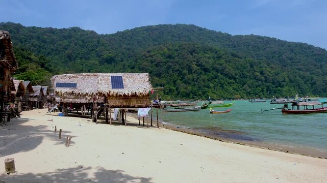 Discover picturesque huts along a tranquil beach in Thailand, surrounded by vibrant green hills and the gentle sounds of waves. Koh Surin Island. Moken Gypsey village