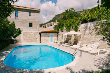 Oval swimming pool with sun loungers behind a stone fence in the courtyard