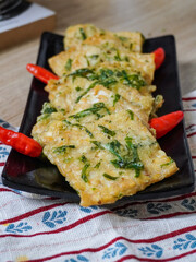 Tempe Mendoan: Indonesian fried tempeh with chili, served on a black plate with a patterned cloth