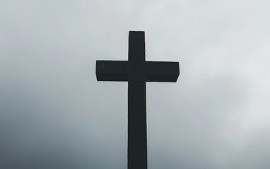 A black cross stands on a hill under a cloudy sky.