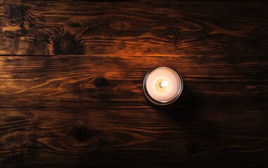 A lit candle rests on a wooden table, casting a warm glow in the surrounding space.