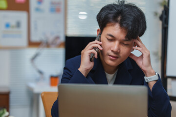 Focused young man multitasking with a phone call and laptop. He is concentrating on work, possibly...