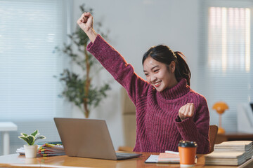 Joyful woman in a cozy office environment celebrating success, raising her fist in triumph while...