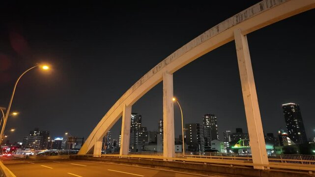 大阪府大阪市大正区、木津川にかかるアーチ状の橋の夜景。都市の光に照らされた橋と建物が、幻想的な雰囲気を演出する定点映像。