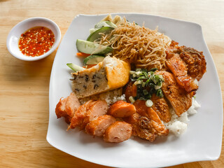 A plate of Vietnamese broken rice (Cơm Tấm) with grilled pork, shredded pork skin, steamed egg meatloaf, pickled vegetables, and chili fish sauce on the side