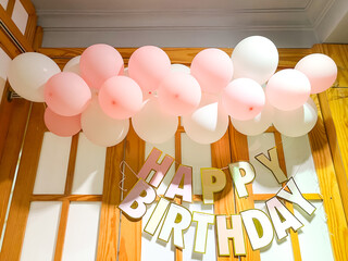 A birthday setup with pink and white balloons and a 'HAPPY BIRTHDAY' banner