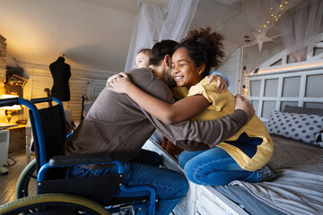 Multiethnic, diverse daughters and single father in a wheelchair sharing a warm moment at home