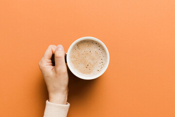 Minimalistic style woman hand holding a cup of coffee on Colored background. Flat lay, top view cappuccino cup. Empty place for text, copy space. Coffee addiction. Top view, flat lay