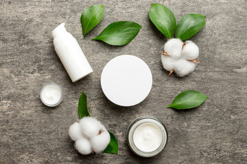 Organic cosmetic products with cotton flower and green leaves on cement background. Flat lay