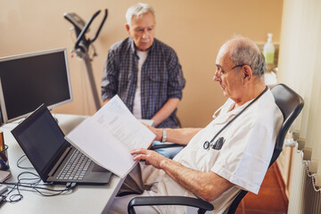 Fototapeta premium Elderly patient is having exam at cardiologist. Doctor is looking at his medical files.