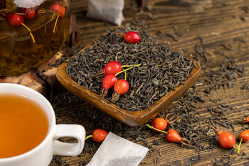red rosehip fruits and hot green tea in a transparent teapot