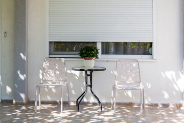  Cozy outdoor patio with table, chairs, and plant under soft dappled sunlight, perfect for serene relaxation.