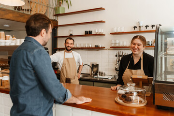A female owner and a male employee stand and laugh while a customer stands across from them, in a cafe