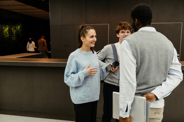 A female employee and a male intern stand and smile while looking at a male employee standing next...