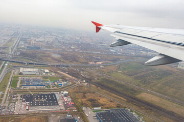  Airplane wing view over sprawling cityscape and industrial zone during flight approach on overcast...