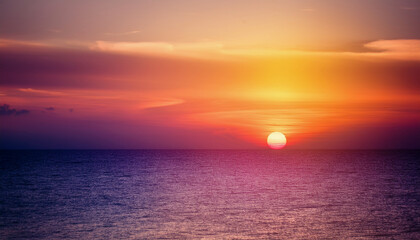 Naklejka premium A breathtaking sunset paints the sky in vivid orange, pink, and purple hues, casting a warm glow over the calm ocean.