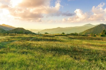 Fototapeta premium beautiful green valley with green fields with green spring grass with nive hills and mountains and scenic colorful cloudy sunset on background of landscape