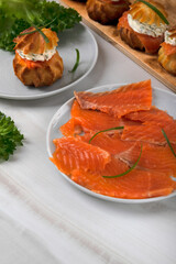 Smoked trout fillet thinly sliced ​​on a ceramic plate. Profiteroles with salted trout and dill cream cheese on the back. Festive appetizer, buffet platter