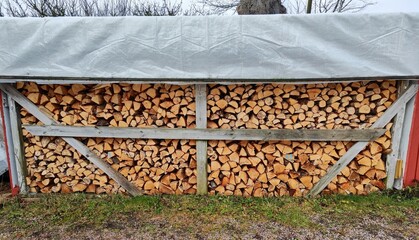 Stacked firewood under protective cover in firewood shed