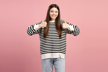 Young girl showing thumbs up with both hands on pink background
