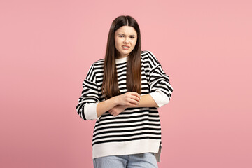Young girl scratching itchy arm suffering from skin irritation on pink background