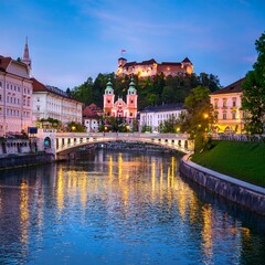 Naklejka premium A stunning evening view of Ljubljana with its riverfront, Triple Bridge, and the illuminated Ljubljana Castle.