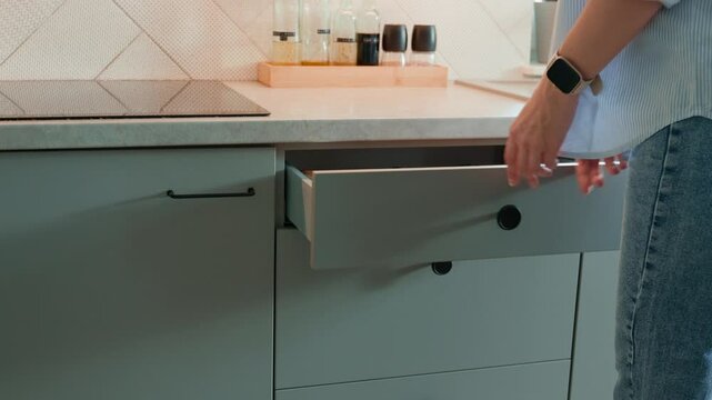 Person opens a kitchen drawer with various utensils in wooden cutlery tray. Woman opening kitchen cabinet. Concept of home organization and functionality interior