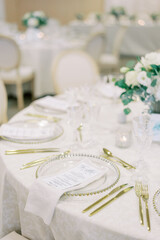 Festive menu on a plate surrounded by golden cutlery on the table