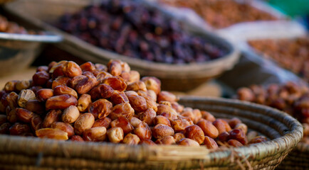 A pile of fresh dates in a woven basket with various types of dried dates in the background at a market.