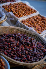 A close-up of dark, glossy dates piled in a woven basket with more dates in the background at a market.