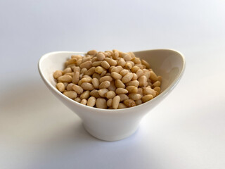 A small white ceramic bowl filled with raw pine nuts