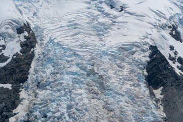 Drone shot of a rugged glacier with deep icy crevasses and snow-capped peaks in a mountainous region