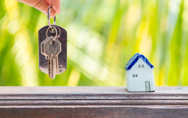 Miniature house with key in girl hand over blurred natural green background, property and real estate business concept