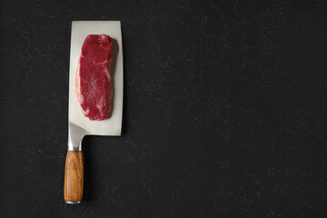 Fresh raw beef meat on a cleaver on a dark kitchen countertop