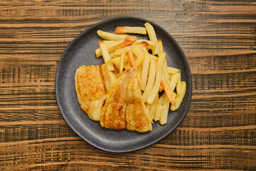 Crispy fried fish fillet served with golden french fries on a wooden table