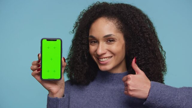 Smiling woman holding smartphone with green screen on blue background