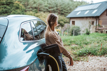 Woman charging electric car, leaning against vehicle with charger in charging port.