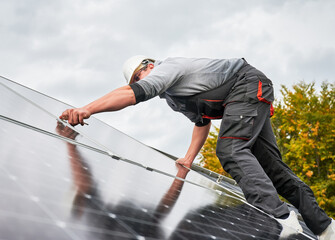 Man electrician mounting photovoltaic solar panels on roof of house. Engineer in helmet installing...