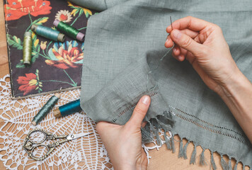 Hands meticulously working on openwork embroidery on grey fabric, surrounded by vintage scissors,...