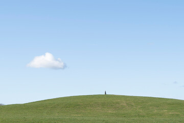Standing stone on green grass hill against a clear blue sky with a cloud.