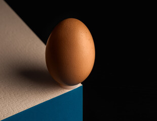 Egg, balancing on table edge. Minimalistic egg stands on colorful table softly illuminated. Simplicity and purity basic ingredient in a balanced diet