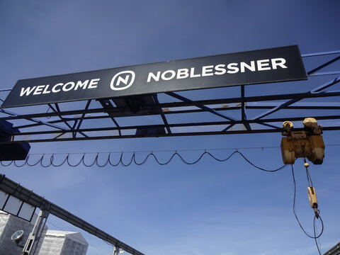 Close up of yellow industrial crane hook (winch) towards blue clear sky. Iron, metal structure. Sign Welcome Noblessner, Tallinn, Estonia, Europe. April 2022