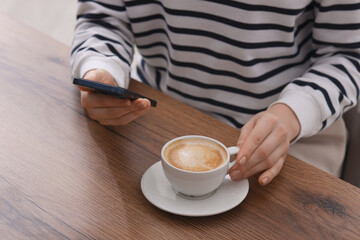 Woman using smartphone during coffee break at wooden table indoors, closeup