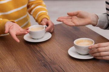 Coffee break. Women with cups of hot drinks at wooden table indoors, closeup