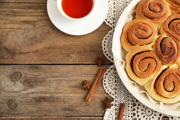 Freshly baked cinnamon rolls, tea and spices on wooden table, flat lay. Space for text